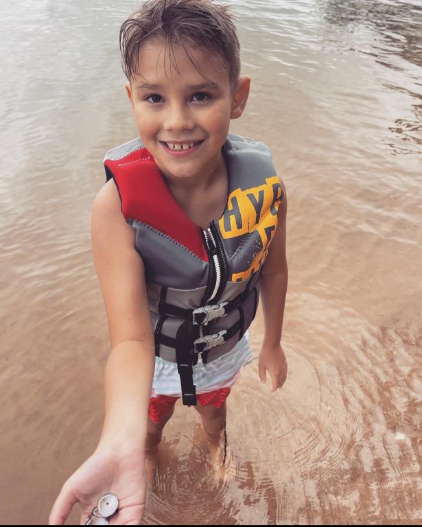 Asher Coleman standing in a lake displays a seashell