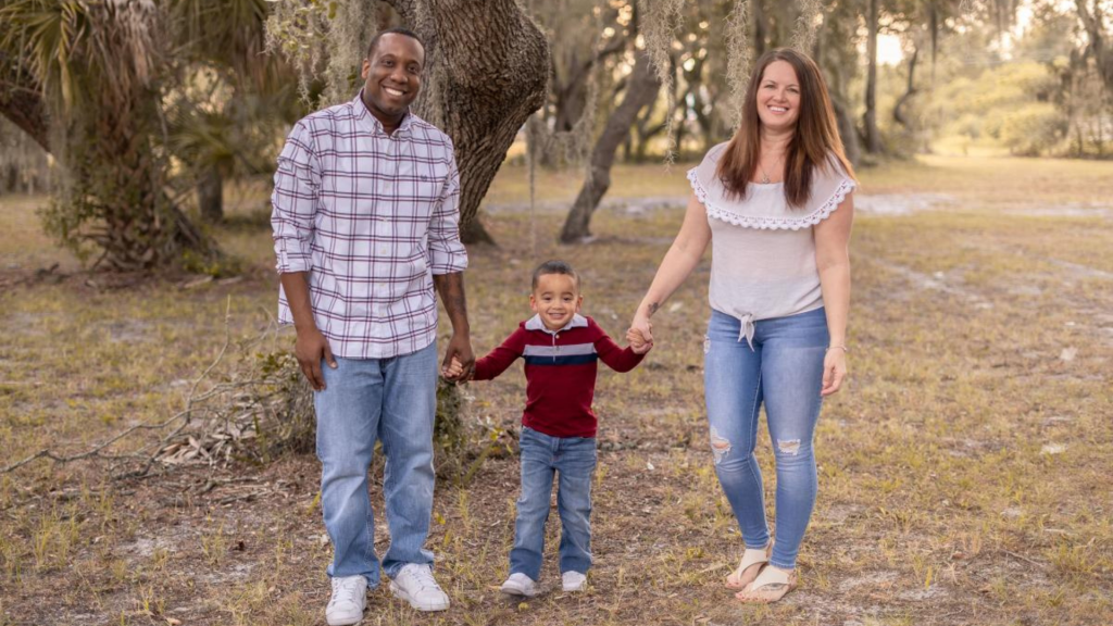 father, child, and mother standing under a tree