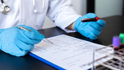 Technician holds vial of blood while checking paperwork.