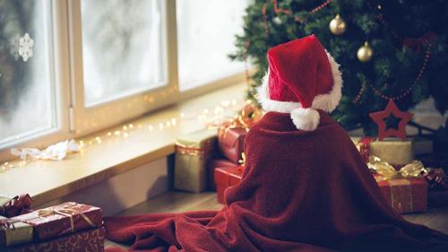 Kid with Santa hat sitting in front of a Christmas tree.